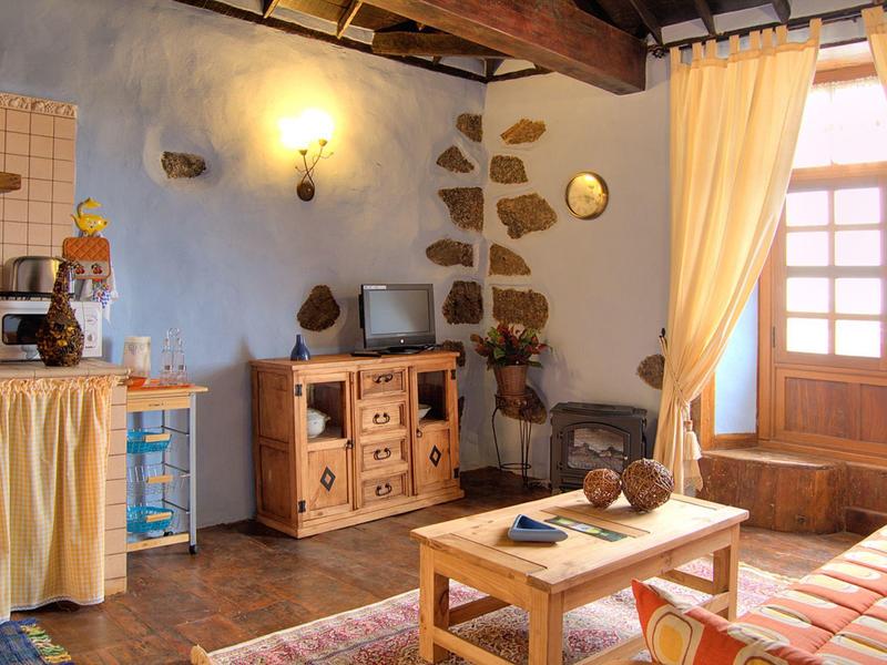 Gemütliches Wohnzimmer mit Holzbalken, Holzmöbeln, blauen Wänden und großen Fenstern mit Vorhängen.