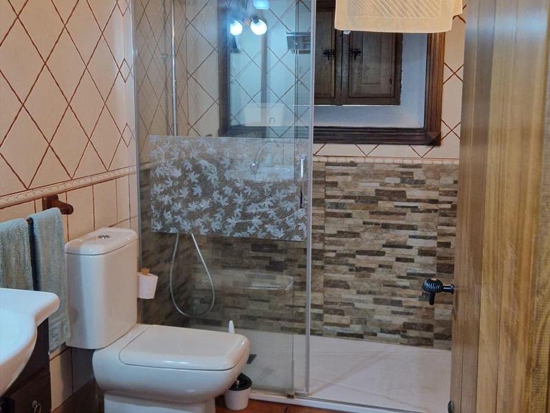 Gemütliches Badezimmer mit Holzbalkendecke, Glas-Duschwand, Keramikfliesen und weißer Sanitärausstattung.