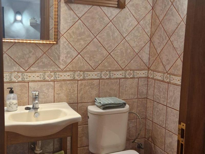 Kleines Bad mit braunen Wandfliesen, weißem WC, Waschbecken und Holzmöbel mit Spiegel.