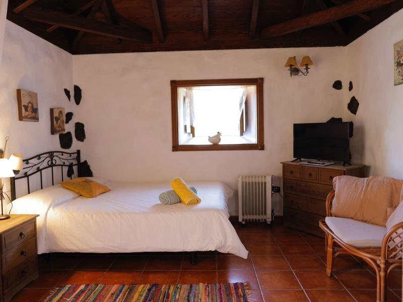 Romantisches Schlafzimmer mit massivem Holzstuhl, Holzboden, bunter Teppich und weißem Bett.