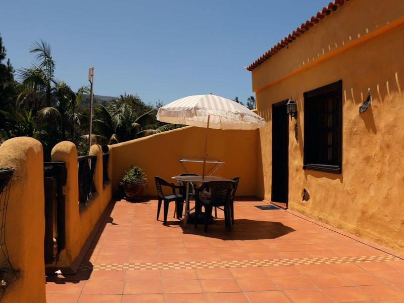 Große Terrasse mit roten Fliesen, gelben Wänden, Tisch, Stühlen und weißem Sonnenschirm.