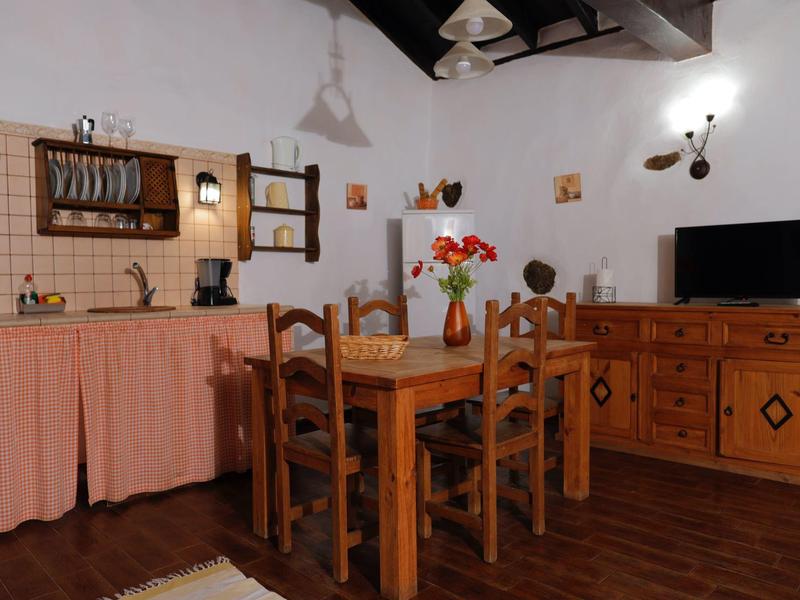 Küche und Esszimmer mit Holzmöbeln, Ziegelboden, Tisch, Stühlen und Küchenschränken mit Vorhängen.