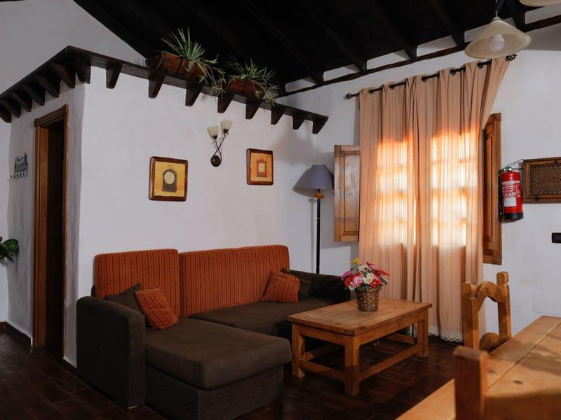 Gemütliches Wohnzimmer mit braunem Sofa, Holzmöbeln, Pflanzen und warmen Vorhängen.