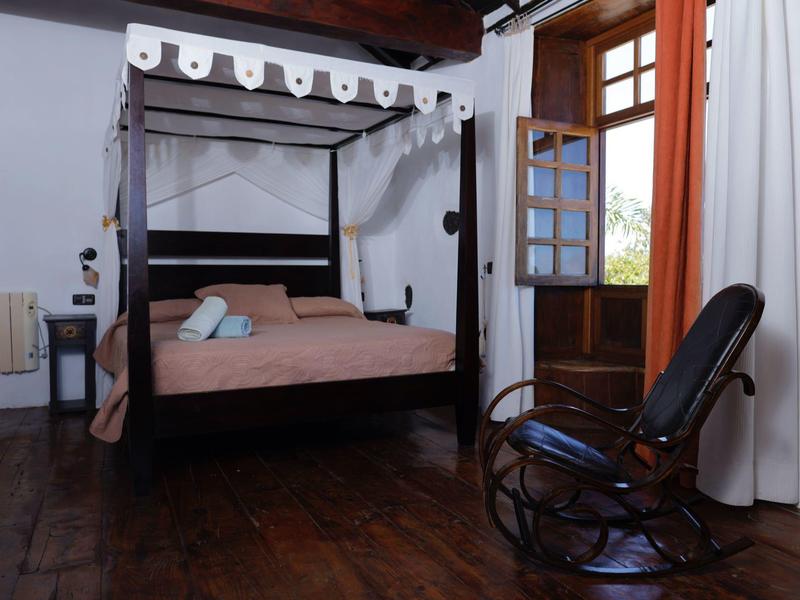 Gemütliches Schlafzimmer mit Himmelbett, Holzboden, Schaukelstuhl und offener Balkontür.