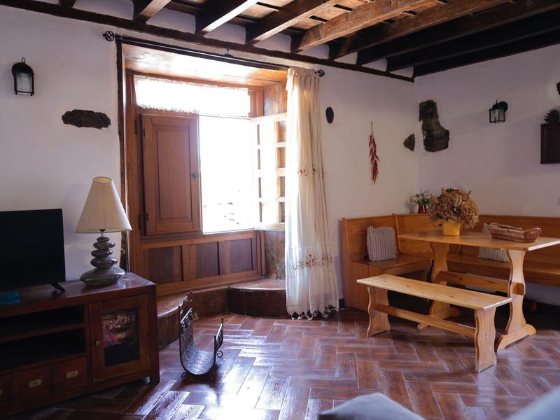 Helles Wohnzimmer mit Holzbalkendecke, offener Tür, Holzmöbeln und Fliesenboden.