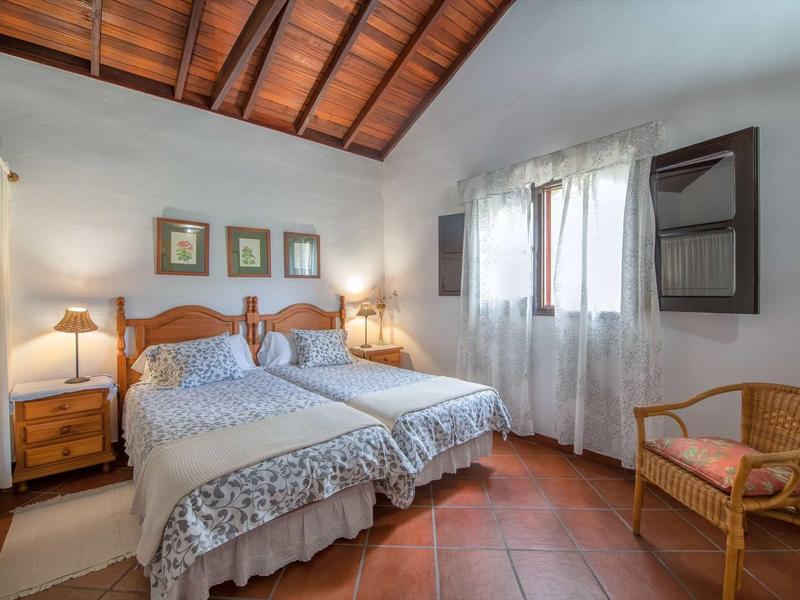 Camera accogliente con due letti singoli, soffitto a travi in legno e pavimento in piastrelle rossicce.