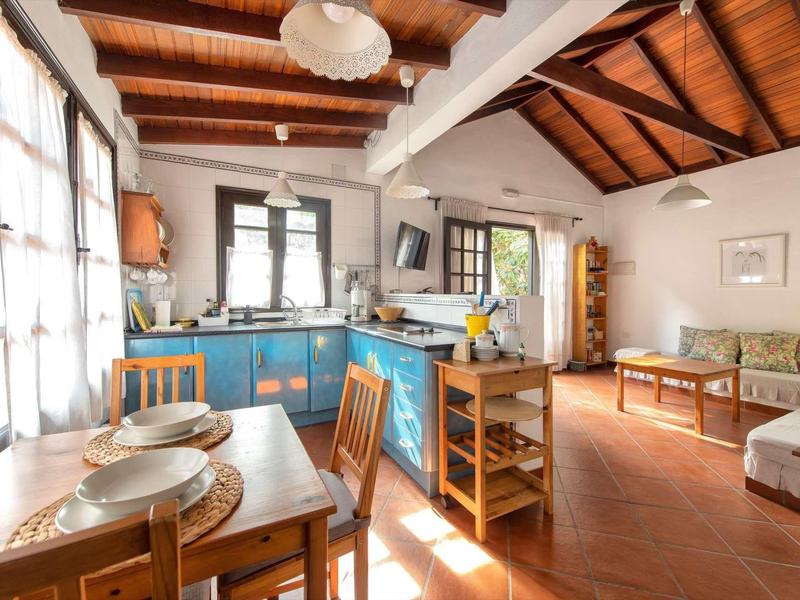 Soggiorno luminoso con soffitto a travi in legno, angolo cottura, tavolo da pranzo e zona salotto con divano