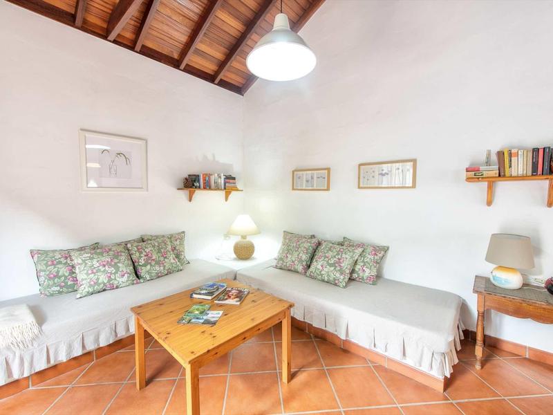 Soggiorno luminoso con divani bianchi, tavolo in legno e cuscini decorativi sotto soffitto con travi in legno.