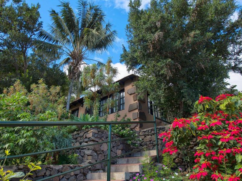 Una scala in pietra con ringhiera conduce a una casa circondata da alberi sotto un cielo azzurro.