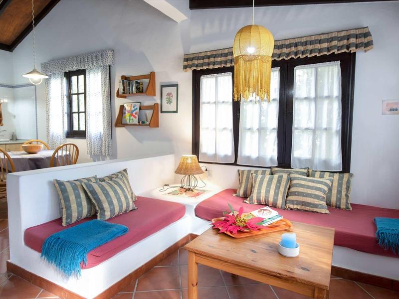 Soggiorno accogliente con divani bianchi, cuscini colorati e tavolo in legno in ambiente luminoso.