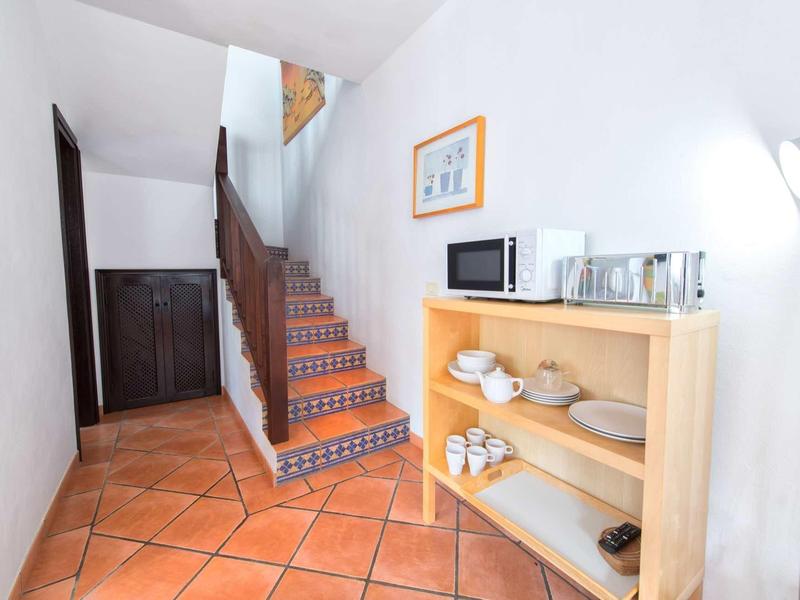 Corridoio con pavimento piastrellato, scala in legno e scaffale con stoviglie e microonde.