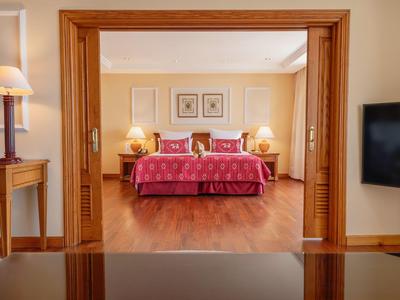 Chambre d'hôtel avec lit double, couvertures rouges, tables de nuit et sol en bois chaleureux.