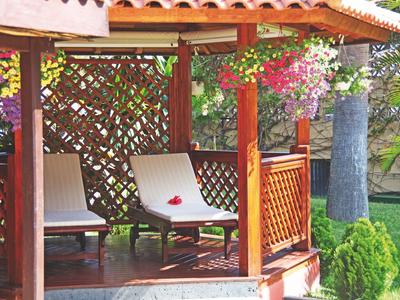 Wooden gazebo with white lounge chairs and hanging flower pots in garden
