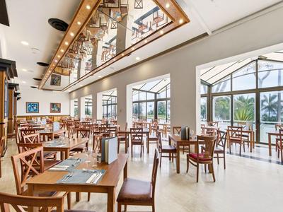 Restaurante moderno y luminoso con sillas de madera y grandes ventanas con vista a palmeras.