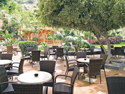 Outdoor café area with tables and chairs under trees and palm plants.