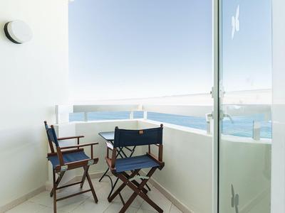 Balkon s dvěma dřevěnými židlemi a výhledem na moře za slunečného dne.