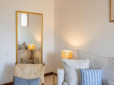 Světý obývací pokoj s béžovou pohovkou, dřevěnou židlí, stojací lampou a stropním ventilátorem s dřevěnými lopatkami.