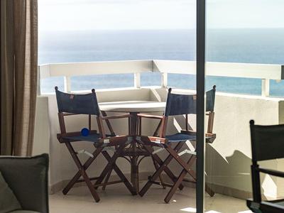 Balkon se stolem a židlemi s výhledem na moře, uvnitř viditelná pohovka a židle.