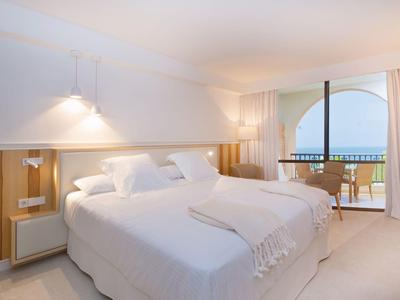 Chambre d'hôtel moderne avec lit double, accents en bois et balcon avec vue sur la mer.