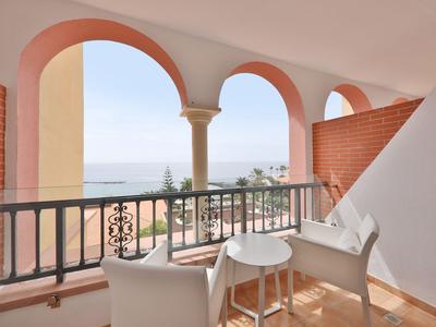Balcon avec mobilier blanc et colonnes donnant sur la mer et des palmiers.