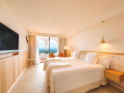 Chambre d'hôtel lumineuse avec deux lits, TV et balcon avec vue sur la mer.