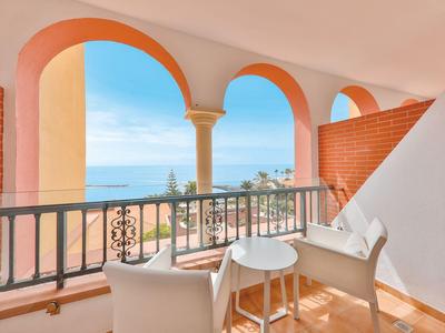 Balcon avec fauteuils blancs et petite table, vue sur la mer et le ciel à travers des arches.