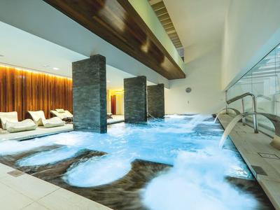 Piscine intérieure moderne avec zones d'eau bouillonnantes et chaises longues dans un cadre élégant.