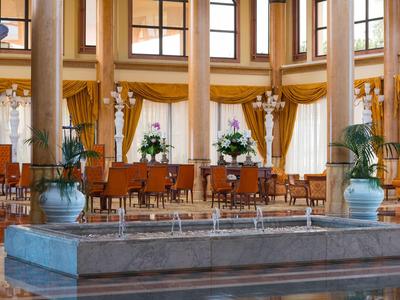 Grand espace intérieur avec fontaine, colonnes et coin salon avec chaises et arrangements floraux.
