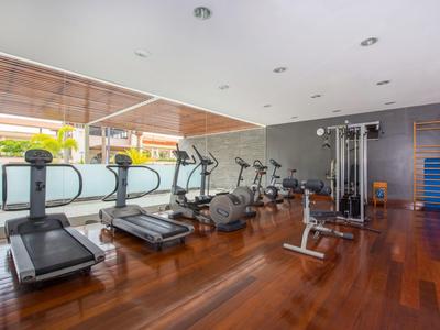 Salle de sport moderne avec tapis roulants et équipements d'exercice sur parquet et grandes fenêtres.