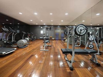 Salle de sport moderne avec sol en bois, miroirs et divers équipements d'entraînement.