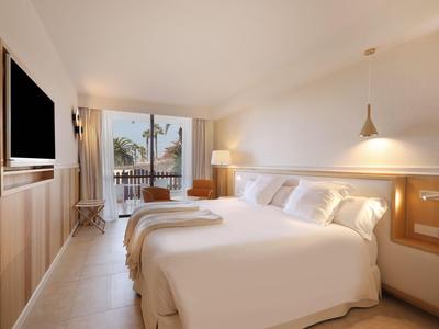 Chambre d'hôtel lumineuse avec deux lits, télévision et balcon avec vue sur des palmiers.