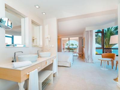 Espace salle de bain lumineux avec deux lavabos et vue sur la chambre et le balcon avec vue sur la mer.