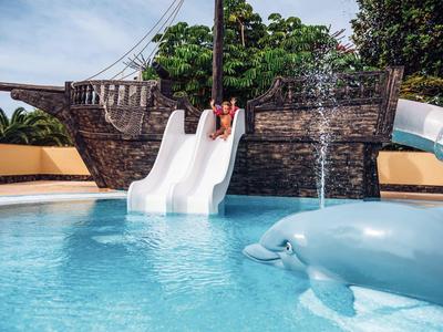 Enfant sur un toboggan blanc menant à une piscine avec une statue de dauphin.