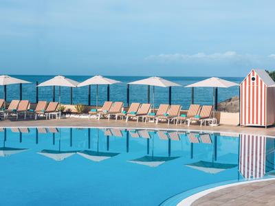 Grand piscine avec parasols et chaises longues face à la mer par temps clair.