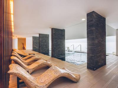 Piscine intérieure avec plusieurs chaises longues et piliers sombres dans un spa moderne.