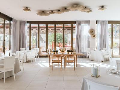 Salle à manger moderne et lumineuse avec tables en bois, chaises blanches, grandes fenêtres et lumière naturelle.