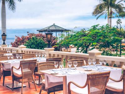 Terrasse élégante avec tables à manger et vue sur la mer dans un hôtel tropical.