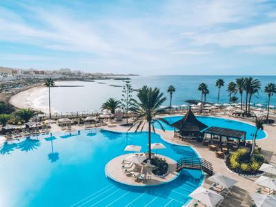 Grand piscine extérieure avec parasols et palmiers au bord de la mer sous un ciel nuageux