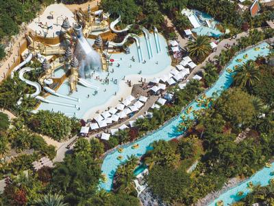 Vue aérienne d'un parc aquatique avec piscine, toboggans et arbres environnants.