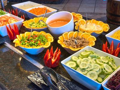 Bunte Salatbar mit Gurken, Möhren, Tomaten, Mais und diversen Dressings in Schalen.
