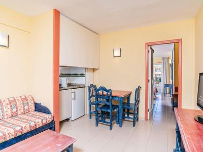 Helles Wohnzimmer mit gelben Wänden, blauem Esstisch, Sofa mit gemustertem Stoff und Flachbildfernseher.