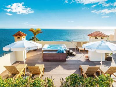Terraza en la azotea con tumbonas, sombrillas y jacuzzi con vista al mar.