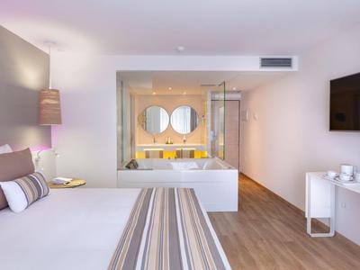 Nowoczesny pokój hotelowy z dużym łóżkiem, wanną i podwójną umywalką w tle.