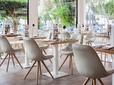 Jasno urządźona restauracja z białymi krzesłami i drewnianymi stołami w jasnej atmosferze.