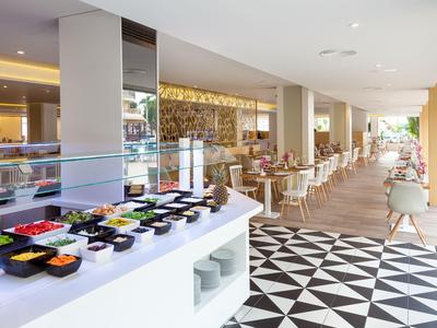 Nowoczesna restauracja z bufetem i stołami w jasnej, otwartej przestrzeni z wzorzystą podłogą.