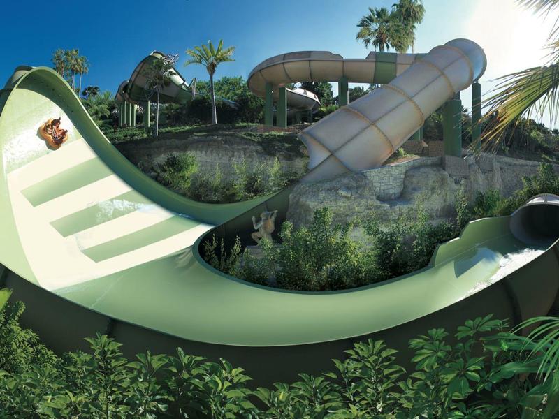 Grande scivolo d'acqua grigio in un parco tropicale circondato da vegetazione rigogliosa.