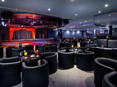 Modern lounge with black armchairs and stage with red curtains in the background.
