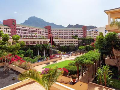 Large multi-story hotel with garden and pool in sunny mountain landscape