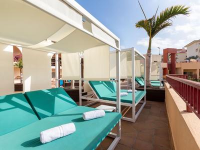 Several green sun loungers with white towels on a covered hotel terrace.