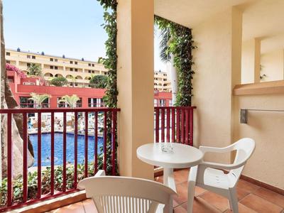 Balcony with table and chairs overlooking a pool and hotel buildings